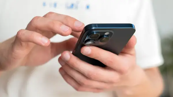 Dłonie trzymające ciemny iPhone, na którym można sprawdzić numer IMEI.