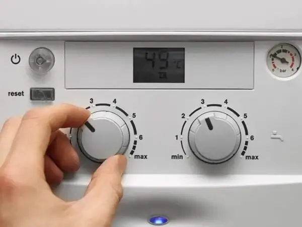 Ręka kręci pokrętłem pieca gazowego dwufunkcyjnego, ustawiając temperaturę. Wyświetlacz pokazuje 49°C.