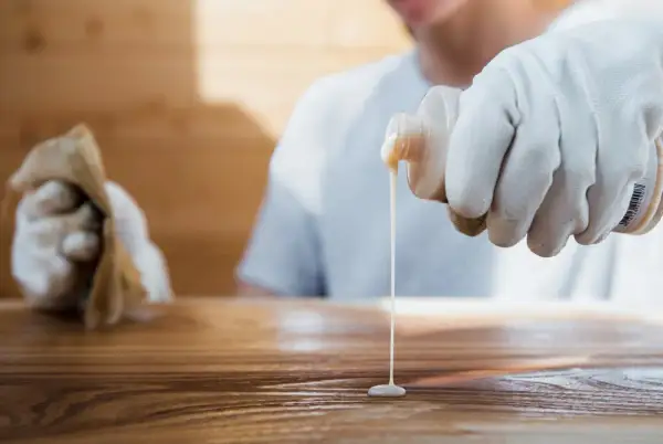 Application d'un produit sur un bois, peut-être pour effacer une tache blanche laissée par un plat chaud.