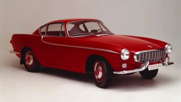 Une élégante Volvo rouge, un modèle emblématique des années 50, se dresse fièrement sur un fond neutre.