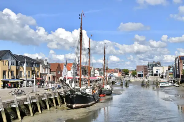Tre segelfartyg ligger vid kaj i Husum, Tyskland. Bakom dem syns en rad hus och en bro över kanalen.
