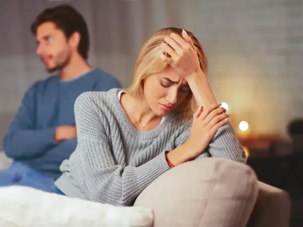 Una mujer angustiada en primer plano, con un hombre de espaldas en el fondo. La escena evoca la confusión y el dolor que a veces acompañan a **que es la limerencia**.