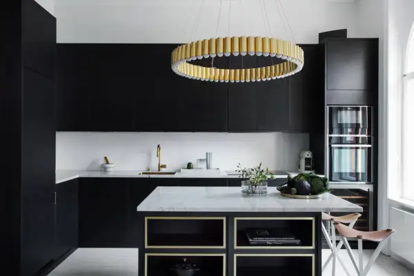 Cucina nera con pareti bianche, isola in marmo, lampadario dorato e sgabelli in pelle.