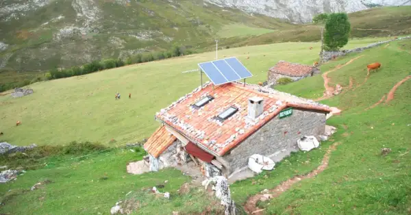 Refugio en Picos de Europa, con paneles solares en el tejado. Vacas pastan en la ladera verde.