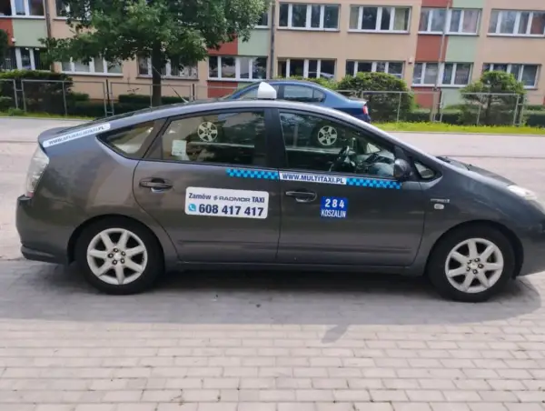 Szary hybrydowy Prius z napisem "284 KOSZALIN" i numerem telefonu do zamówienia taksówki.