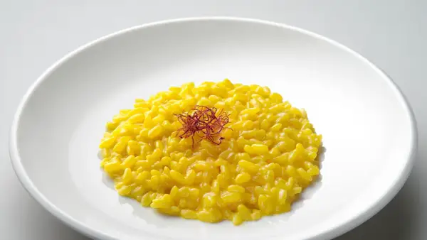 Un cremoso risotto giallo zafferano, guarnito con fili di zafferano, un piatto che promette un riso più leggero e gustoso.