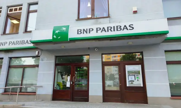 Wejście do placówki banku BNP Paribas z zielonym logo i napisem. Obok drzwi znajduje się bankomat.