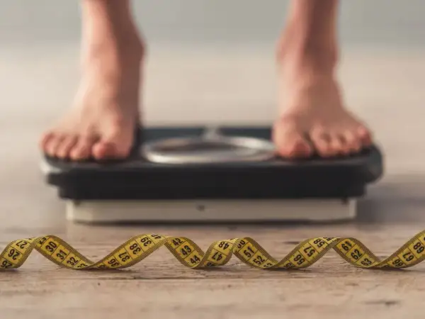 Pieds sur une balance, ruban à mesurer enroulé au premier plan. La question "pourquoi je ne perds pas de poids" résonne.