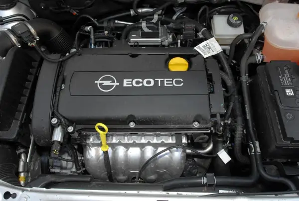 Silnik Ecotec w samochodzie Opel Astra H. Widoczny jest czarny dekiel z logo Opla i napisem Ecotec, żółta miarka oleju oraz elementy układu chłodzenia i dolotowego.