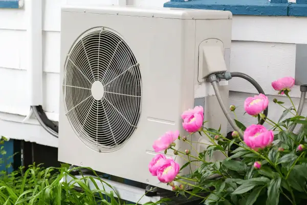 Unità esterna di una pompa di calore ad aria, con fiori rosa in primo piano.