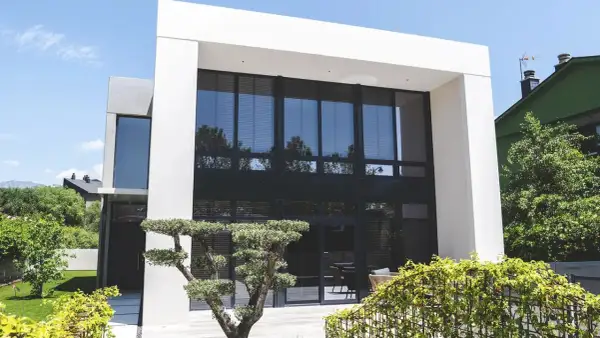 Moderna casa con fachada gris y beige, grandes ventanales y jardín cuidado.