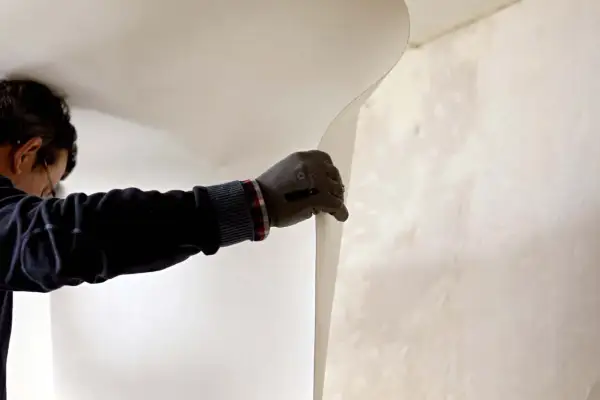 Un ouvrier pose de la fibre de verre dans les angles d'un mur.