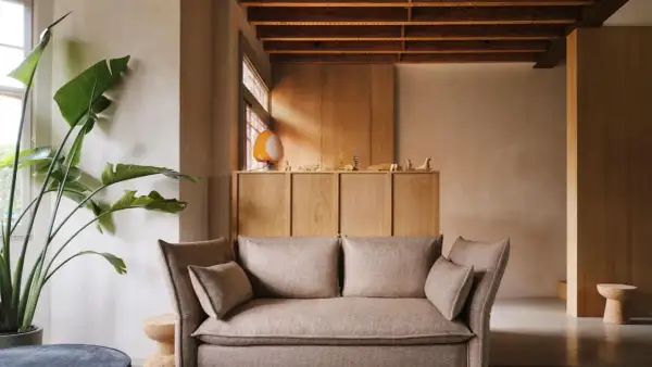 Gemütliches Wohnzimmer mit beigem Sofa, großer Zimmerpflanze und einem Schrank aus hellem Holz, der zum holz streichen einlädt.