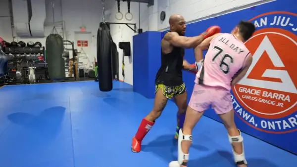 Two fighters practice boxing head movement drills in a gym. One throws a punch while the other dodges.