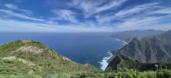 Vista del Roque de Tábarno, un promontorio verde y rocoso que se adentra en el mar azul bajo un cielo nublado.