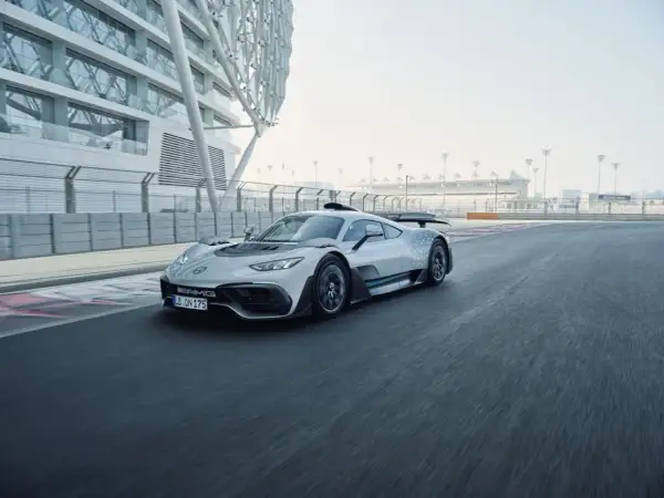 Srebrny Mercedes-AMG Project One pędzi po torze wyścigowym, obok nowoczesnej architektury.