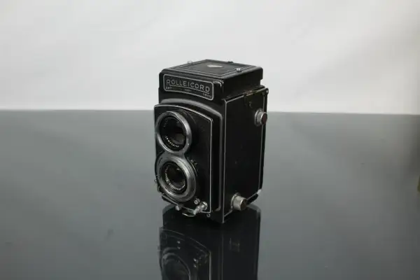 A vintage Rolleicord camera sits on a reflective surface, its twin lenses and classic design hinting at a rich photographic history.