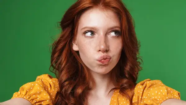 A young woman with fiery red hair, often symbolizing passion and uniqueness, puckers her lips against a vibrant green backdrop.