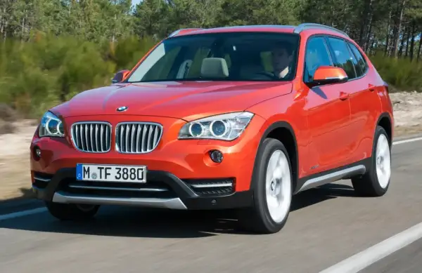 Pomarańczowy BMW X1 E84 jedzie po drodze, za kierownicą siedzi mężczyzna.