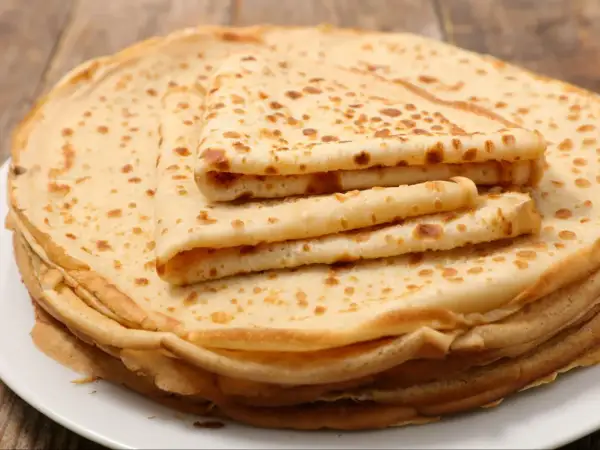 Stos cienkich, lekko zarumienionych naleśników bez jajek, ułożonych na białym talerzu. Idealne na śniadanie lub deser.
