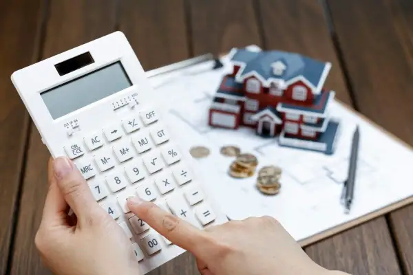 Calculadora en mano, se evalúa cuánto se deduce por alquiler de vivienda, con una maqueta de casa, monedas y planos.