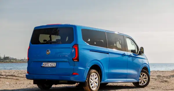 Błękitny VW Transporter T7 na piaszczystej plaży, z widokiem na morze.