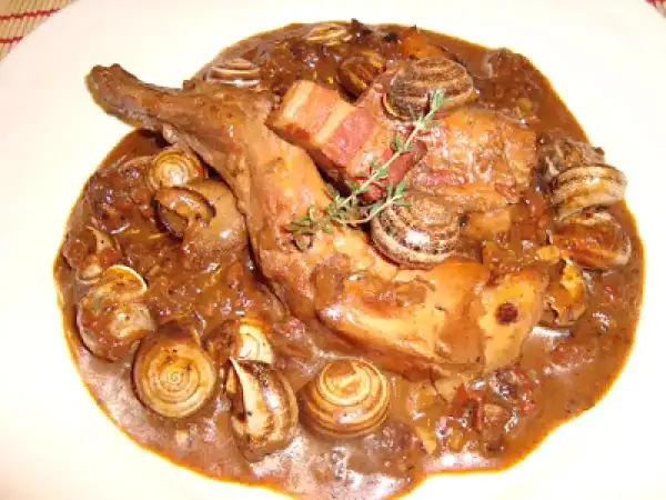 Guiso de conejo con caracoles, bañado en una rica salsa oscura, con trozos de tocino y una ramita de romero.
