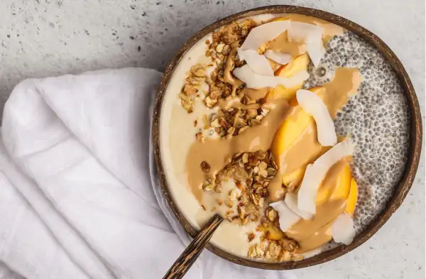 Cremige Chia Overnight Oats im Kokosnussschalen-Bowl mit Pfirsich, Granola und Erdnussbutter. Ein gesunder Start in den Tag!