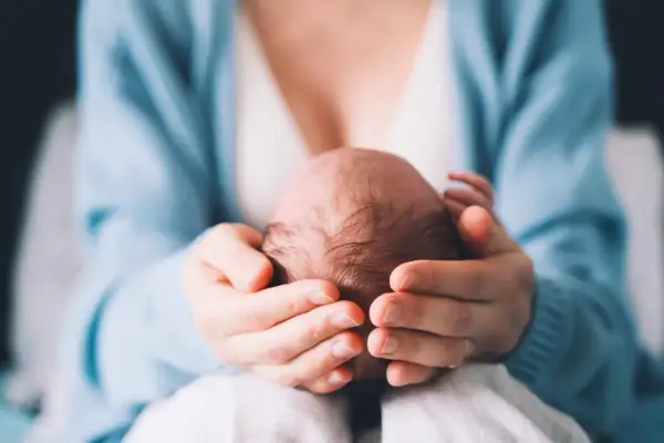 Delikatne dłonie otulają główkę noworodka, ukazując troskę i miłość. Szybko zarastające ciemiączko to naturalny proces, a ten obraz to dowód na to, jak szybko dzieci rosną.