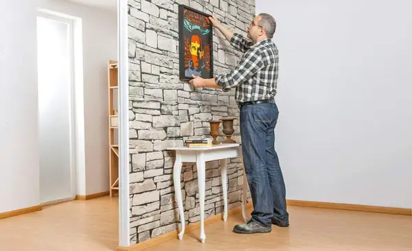Mann hängt Bild an Trockenbauwand. Ein Mann baut eine Trockenbauwand und dekoriert sie mit einem Bild.