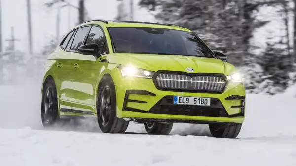 En ljusgrön Skoda Enyaq testas i snö. Bilen kör genom ett vinterlandskap med träd i bakgrunden.
