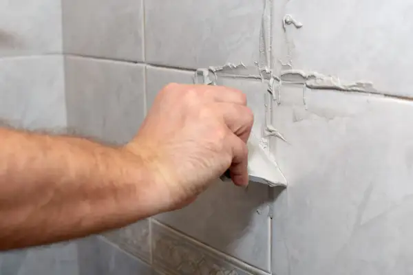 Main tenant utilise une spatule pour refaire le joint du carrelage mural.