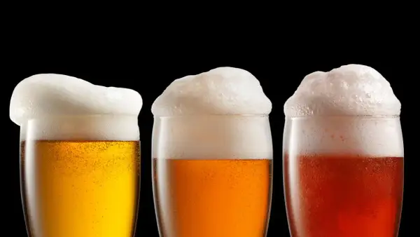 Tre bicchieri di birra con abbondante schiuma, uno biondo, uno ambrato e uno rosso.