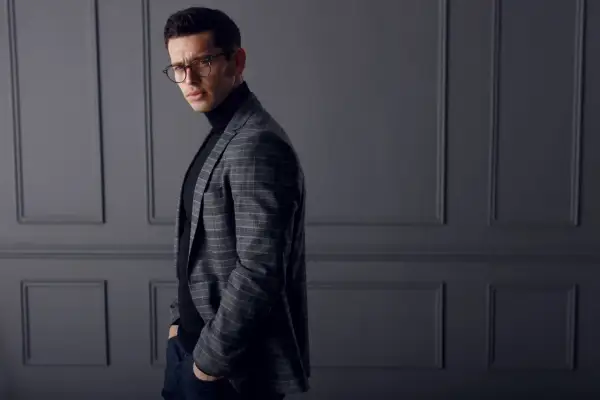 Elegancki mężczyzna w okularach, w kratowaną marynarkę i czarny golf, który stanowi idealny sweter pod marynarkę.