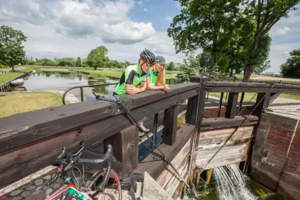 Para rowerzystów odpoczywa przy śluzie, podziwiając malownicze **trasy rowerowe Augustów**.