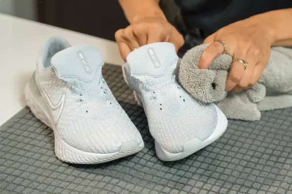 Hands cleaning light blue Nike sneakers with a grey cloth.