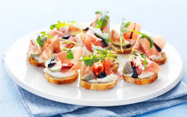 En tallrik med läckra crostini med lufttorkad skinka, färska fikon, krämig ost och ruccola, ringlad med balsamvinäger.