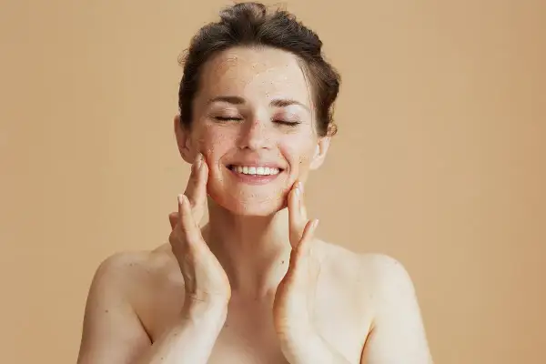 Kobieta z zamkniętymi oczami nakłada peeling na twarz, ciesząc się zabiegiem. Zastanawiasz się, jak często robić peeling twarzy?