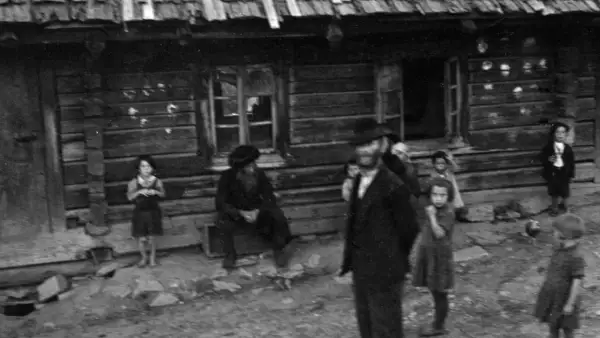 Kinder und Erwachsene stehen vor einem Holzhaus. Die Szene erinnert an die **Judenverfolgung** und die damit verbundene Not.