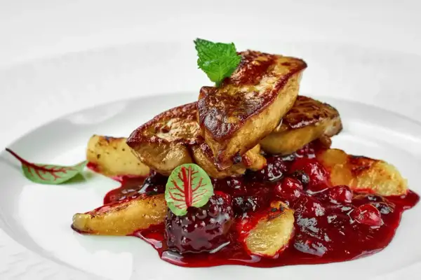 Tranches de foie gras poêlé, nappées d'une sauce aux fruits rouges, garnies d'une feuille de menthe et d'une petite feuille rouge. L'épice foie gras est sublimée par cette présentation.
