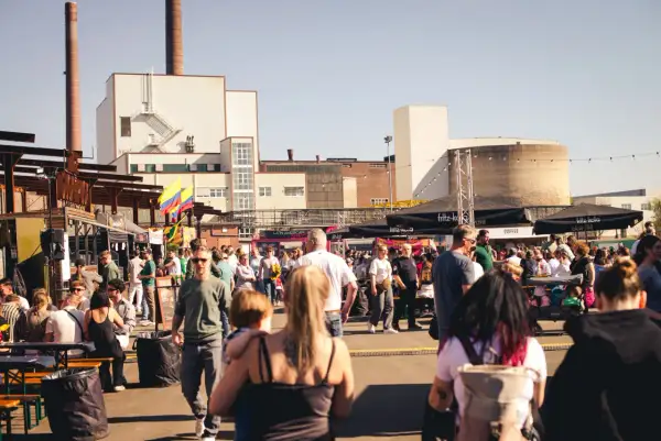 Menschen genießen das Street Food Festival Bergisch Gladbach mit vielen Essensständen und bunter Atmosphäre vor Industriebauten.