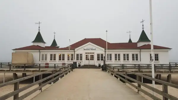 Historyczna budowla na molo w Ahlbecku, z charakterystycznymi zielonymi dachami i białymi ścianami, zaprasza do spaceru.