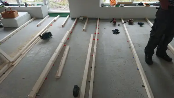 Arbetare förbereder för att regla upp golv med träreglar och verktyg som cirkelsåg och skruvdragare.