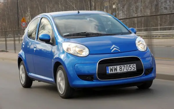 Niebieski Citroen C1 pędzi po drodze, odbijając światła miasta w swoich błyszczących reflektorach.