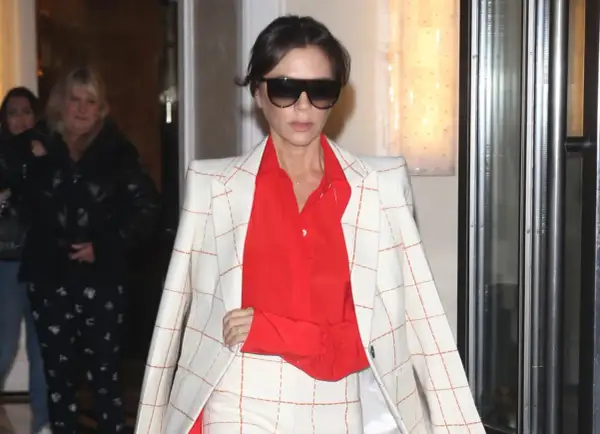 Victoria Beckham, con un traje de cuadros blanco y naranja y camisa roja, sale de un edificio.