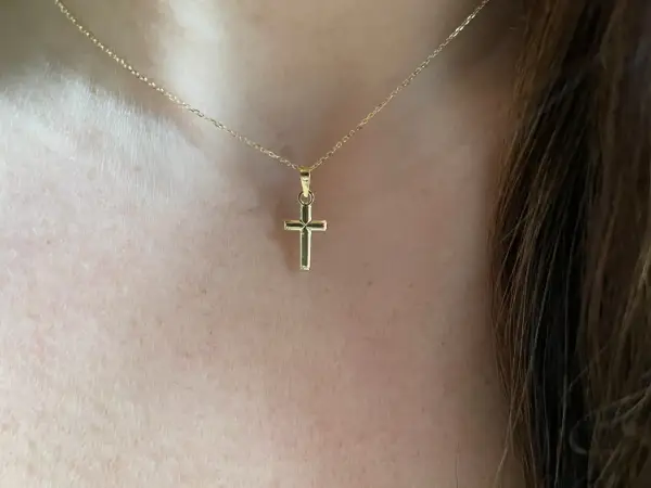 Una delicada cadena de oro sostiene una cruz de oro pequeña, un símbolo de fe y elegancia.