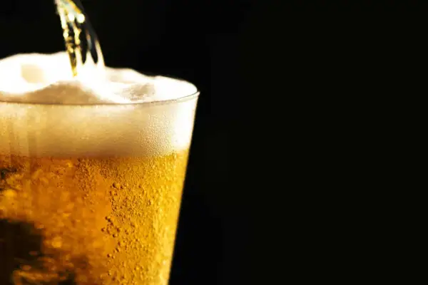 Birra ghiacciata che cola in un bicchiere, creando una schiuma densa e invitante. Le bollicine danzano nel liquido dorato.