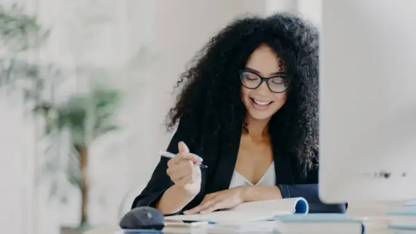 Mujer sonríe mientras escribe, pensando en como empezar una carta de motivación.
