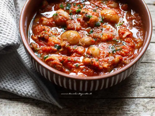 Seppie in padella, succulente e profumate, servite in una ciotola marrone con un contorno di tovagliolo grigio.