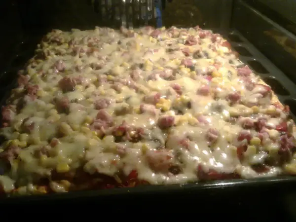 Pyszne ciasto do pizzy z serem, kukurydzą i wędliną, pieczone w piekarniku. Idealne na rodzinny obiad.
